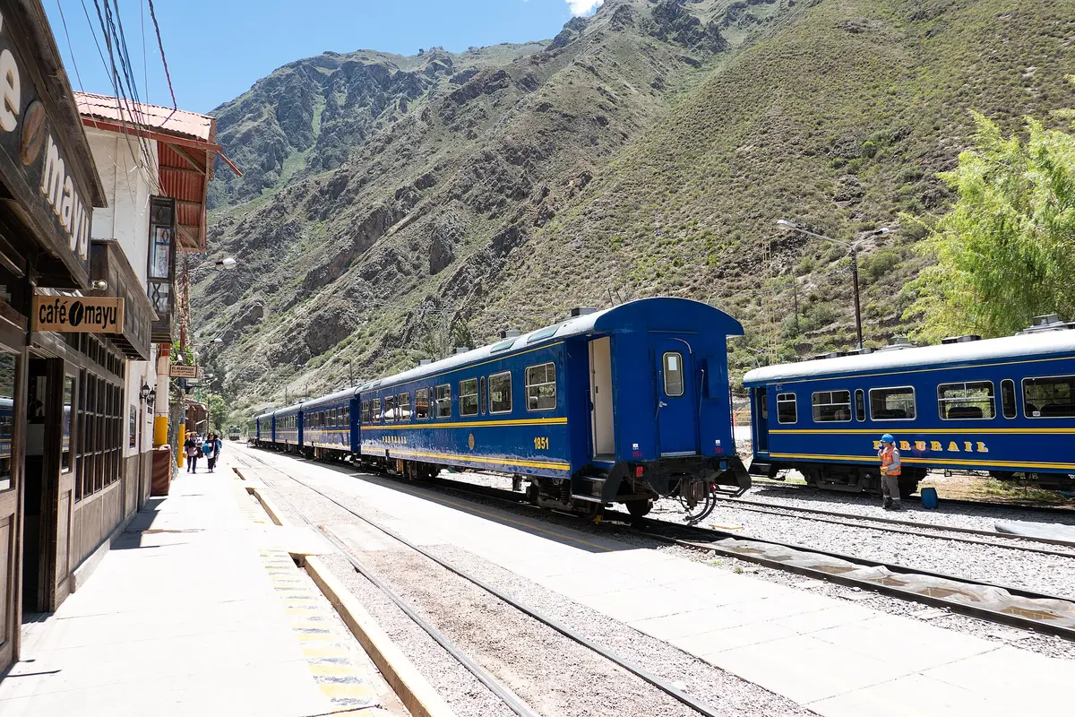 Blaue Zugwagen an einem Bahnsteig im Bahnhof Ollantaytambo, dahinter ein steiler, trockener Berghang